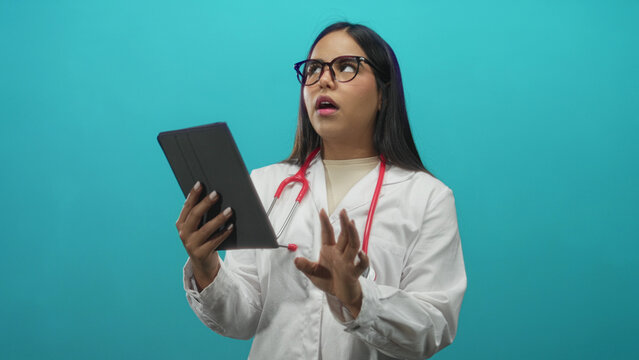 Female doctor in white coat and glasses holds tablet with one hand, red stethoscope around neck, mouth open and head tilted while yawning in studio; fatigue.