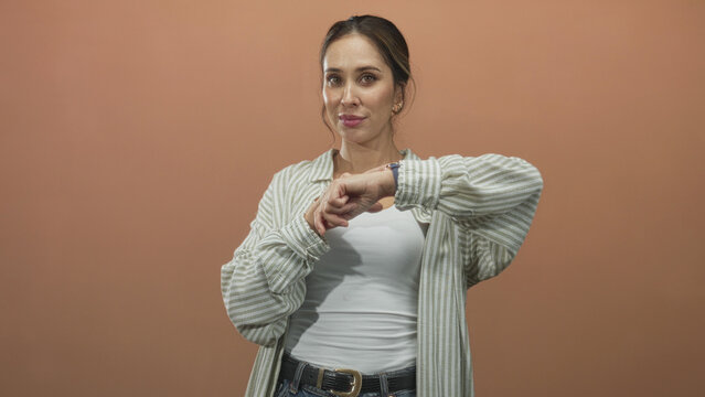 Woman points finger to wristwatch while checking time, casual striped shirt and white tank top visible in studio; impatience punctuality waiting.
