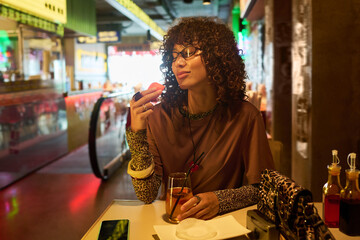 Young adult biracial woman with curly hair enjoying food in cafe with eyes closed. Image represents...
