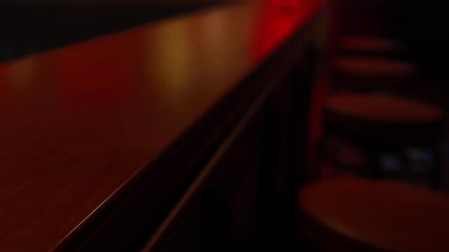 The scene shows an empty bar counter with wooden stools in a dimly lit space. Red lights create a warm atmosphere around the area.