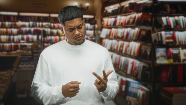 Hispanic man counts on fingers while inspecting ring with furrowed brow in bookstore; confusion reflection.