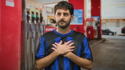 Man in blue football jersey raises right hand palm out and places left hand on chest at a gas station on a street  quiet respect. © Krakenimages.com