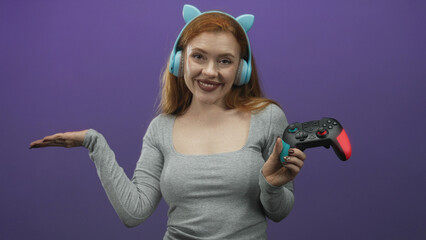 Redhead woman wearing light blue headphones and holding a gamepad with palm up gesture in studio  playful energy. © Krakenimages.com