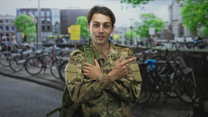 Man soldier in camouflage jacket points finger to shoulder while holding backpack on street  pride duty. © Krakenimages.com