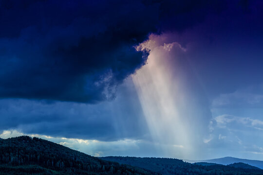 Dramatic sun rays breaking through storm clouds over mountain forest