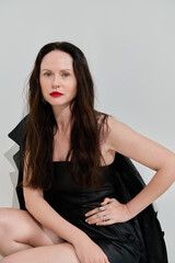 Obraz premium A stunning woman poses in a stylish black dress with striking red lips against a minimal backdrop.