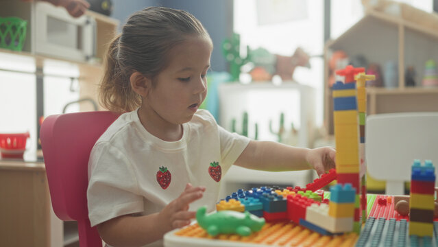 Hispanic girl stacking colorful toy blocks with hand, constructing a tower in a building; concentration learning creativity.