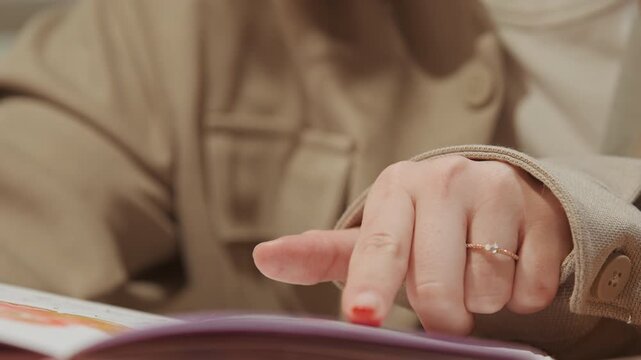 Close up of woman in soft lighting flipping through colorful book pages with her finger revealing textures and details. Her hand movements interact naturally as woman browses open notebook