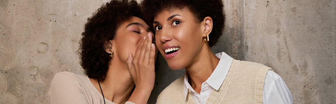 Two young African American women share laughter and secrets, celebrating their friendship.
