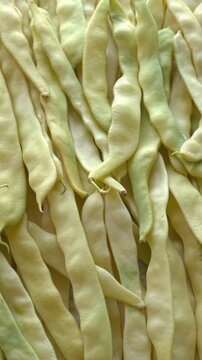 Merveille de Venise yellow pole beans, full-frame background texture. Fresh organic wax bean pods heap, slowly rotating in a tight top view with backlit natural window light, vertical video.