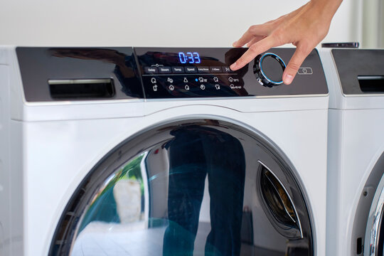 Hand adjusting controls on front loading washing machine with digital timer display