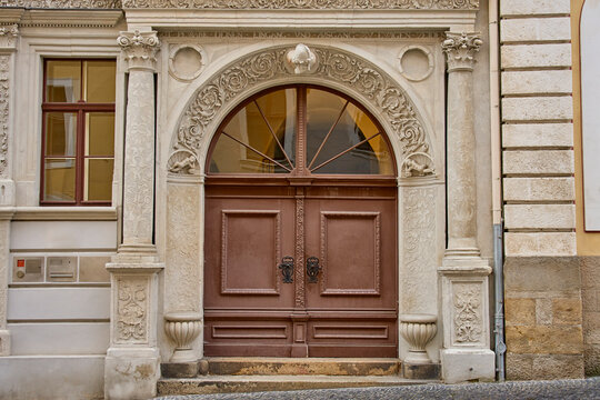 Large wooden double door framed by detailed stone carvings, columns and arched window