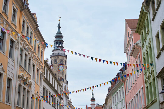 Historic European street with colorful buildings, clock tower and festive flags
