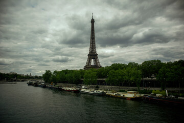 Fototapeta premium A Wide Scenic View of a Famous Iron Lattice Tower next to a River with Moored Boats Under a Cloudy Sky