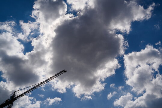 Silhouette of a construction crane jib against dramatic cloudy sky.