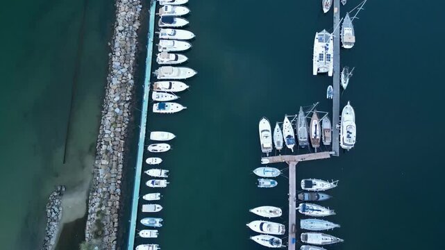 Top-down aerial drone view flying over wooden pier and sailboats moored in rows at harbor marina in Sanremo, Italian Riviera, Liguria, Italy