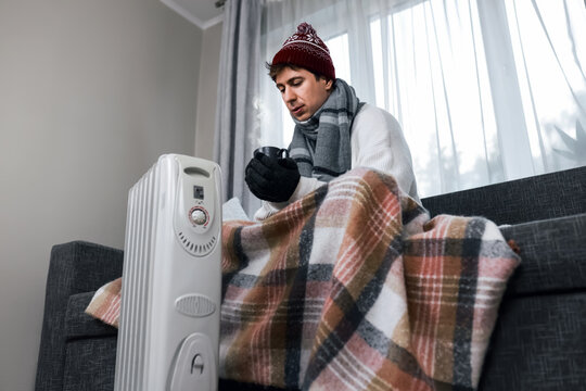 Freezing man indoors at home near a heater during a winter cold snap, facing rising heating costs, energy crisis, and unpaid utility bills