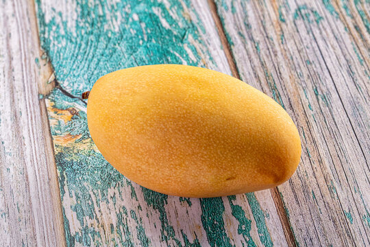 Ripe yellow mango on weathered teal and gray wooden surface