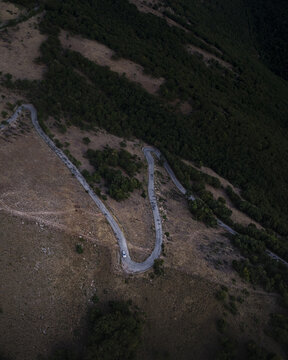 Aerial view of a winding mountain road snaking through the dry hillside landscape with patches of green trees in Spoleto, Umbria, Italy.