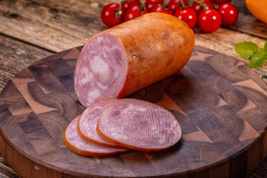 Sliced ham sausage on wooden cutting board with cherry tomatoes and basil