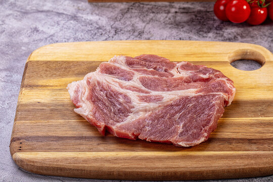 Raw pork neck steak on wooden cutting board with cherry tomatoes in background