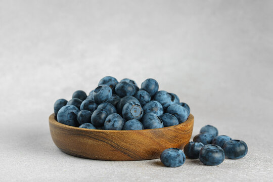 Fresh ripe blueberries in wooden bowl on a light gray textured background. Seasonal summer harvest, healthy food, natural nutrition, wholesome eating and nutritious source of vitamins and antioxidants