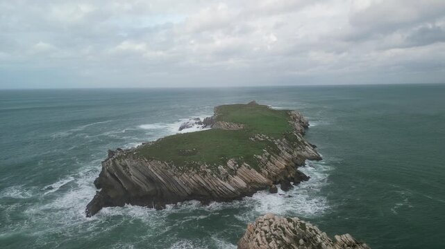 Aerial view of Baleal Island with rocky cliffs, green grass, and crashing waves in the Atlantic Ocean in Peniche, Leiria District, Portugal.