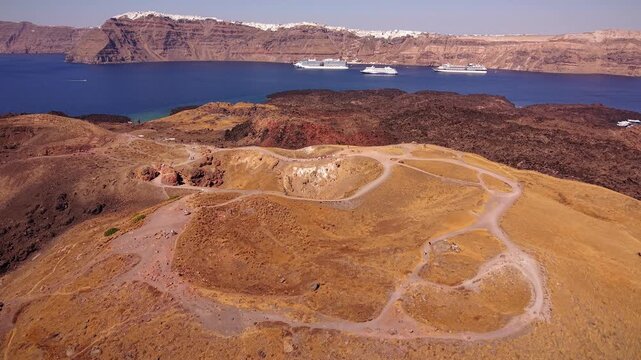 Dynamic aerial drone clip exploring the dark volcanic rocks of Tholos Naftilos, with the vibrant city of Fira resting high on the Santorini caldera edge, Greece.