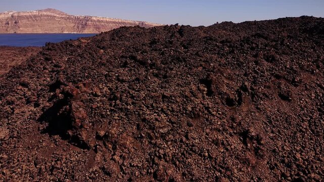 Cinematic aerial drone flight over the rugged Tholos Naftilos crater rim, capturing the unique geology and volcanic landscape of Nea Kameni in Santorini, Greece.