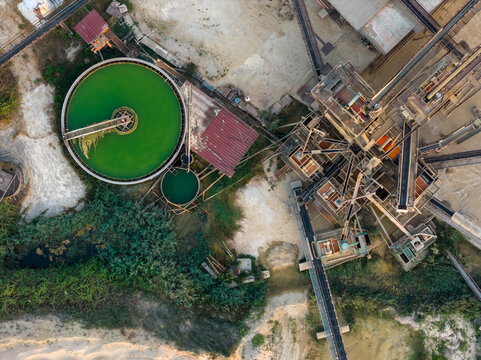 Aerial view of an industrial processing plant featuring a large circular green water treatment tank, conveyor belts, and metal structures in Rome, Lazio, Italy.