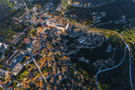Aerial view of the historic town of Capestrano with its dense cluster of stone buildings, narrow streets, and surrounding hilly landscape in Capestrano, Abruzzo, Italy.