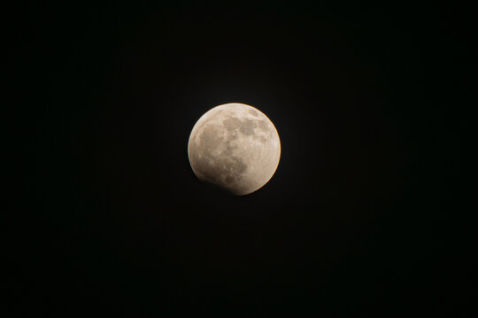 Moon undergoing a partial lunar eclipse, its surface slowly obscured by earth's shadow, creating a celestial phenomenon visible against the dark expanse of space