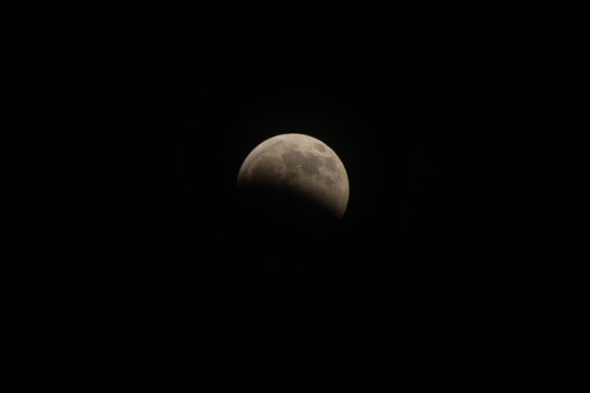 Moon experiencing a partial lunar eclipse, earth's shadow beginning to cover the celestial body, creating a striking astronomical phenomenon in the dark night sky
