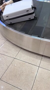 White and beige suitcases traveling around rotating baggage carousel inside modern airport terminal, illustrating luggage collection process, shot handheld. vertical video. High quality 4k footage