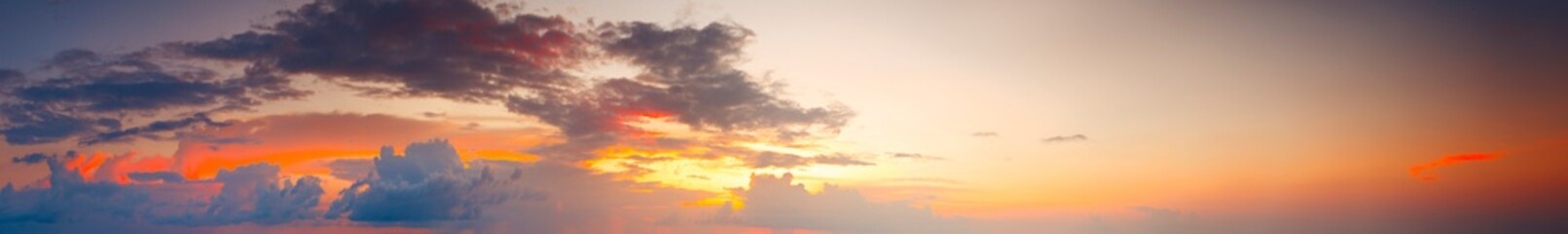 Fototapeta premium Wide Panoramic Sunrise with orange and purple sky hues. Setting sun glows behind scattered clouds. Warm gradients blend into soft horizon tones