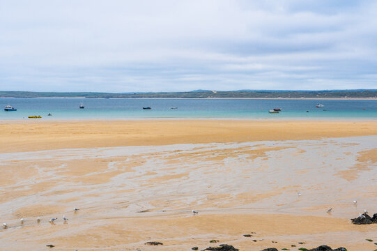 Sandy beach at low tide with turquoise water on an overcast day.
