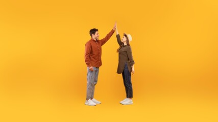 Fototapeta premium Happy Young Man And Woman Engaging In A High Five Gesture, Celebrating A Positive Moment In A Studio With A Yellow Background. Showcasing Joy And Connection, Concept Of Togetherness.
