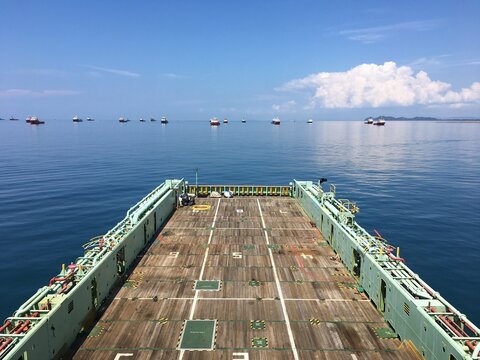 View of the empty main deck of an offshore support vessel with multiple ships anchored in the distance