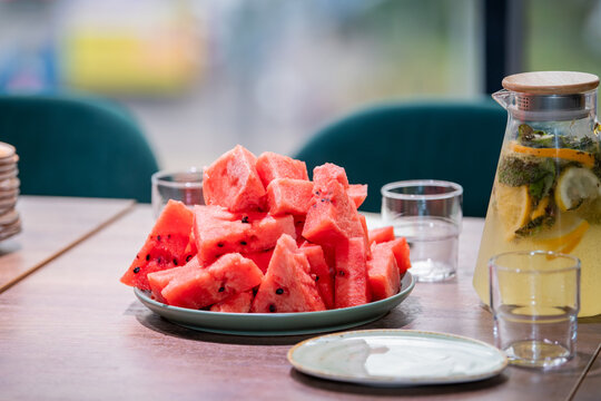 Fresh watermelon slices on plate with lemonade in glass jug on wooden table. Summer healthy snack and refreshing drink. Vitamin fruit dessert for cafe, party or picnic concept.