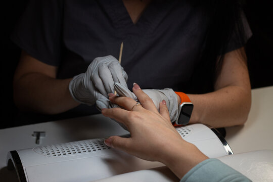 Correcting top coat on nails with orange stick showing precise technician work removing excess material and shaping neat coating