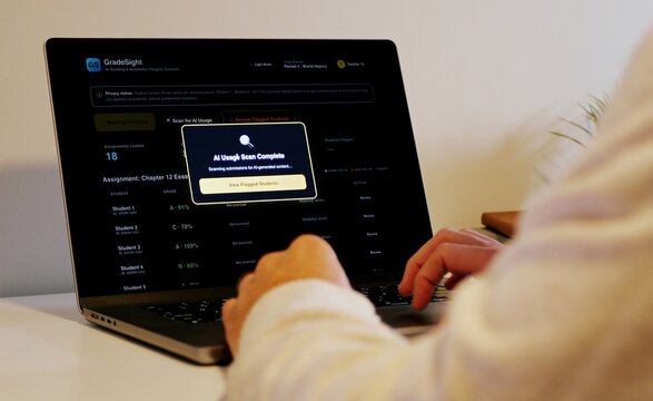 Educator at a laptop using AI software for automated bulk grading of student essays while scanning for unauthorized student AI usage and plagiarism