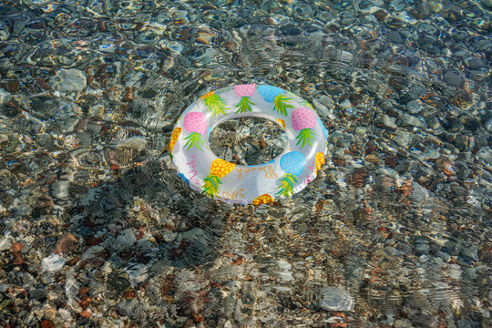Inflatable swim ring floating in clear sea water over pebbles