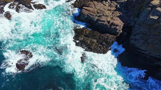 Water splashes over rocks as waves hit the coastline. The sun shines on the ocean, creating bright blue water around the shores. This scene captures the power of the sea.