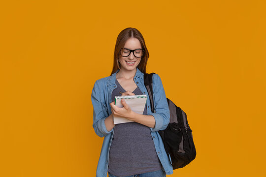 College student writing notes in notebook with backpack