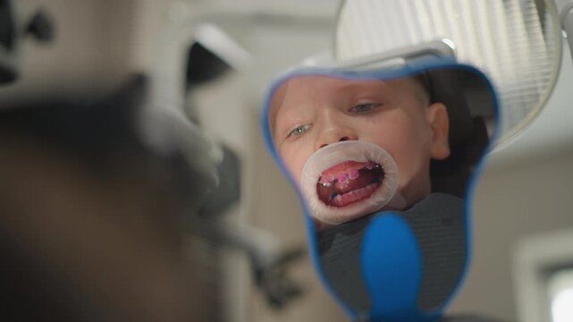 Close up of young boy in orthodontic dental chair with his mouth open revealing pink braces and teeth. scene is set inside well lit modern clinic featuring medical equipment like overhead