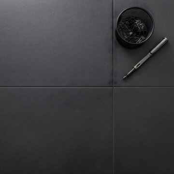 Top-down flat lay view of dark charcoal grey ceramic floor tiles styled with a black fountain pen and a wire mesh holder with binder clips