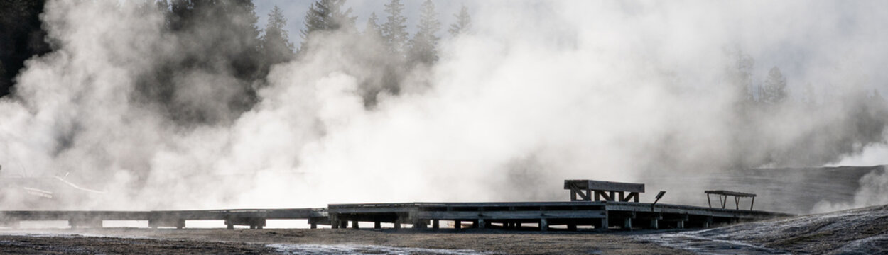 Early morning walk in upper geyser basin and Old Faithful steaming geothermal features, wood boardwalk and lonely empty bench, summer vacation at Yellowstone National Park
