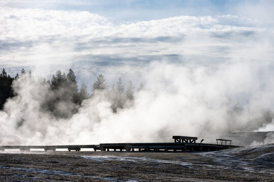 Early morning walk in upper geyser basin and Old Faithful steaming geothermal features, wood boardwalk and lonely empty bench, summer vacation at Yellowstone National Park
