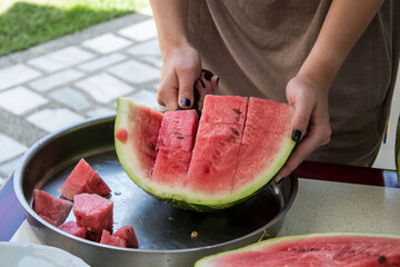 Fresh watermelon being cut into pieces outdoors with bright red fruit and green rind. Juicy slices placed in a bowl create a vivid summer scene suitable for food, freshness and seasonal themes. © Mati