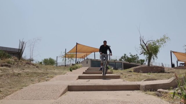 Determined cyclist riding a mountain bike down concrete stairs in a city park, demonstrating skill and balance in an extreme urban cycling challenge in slow motion